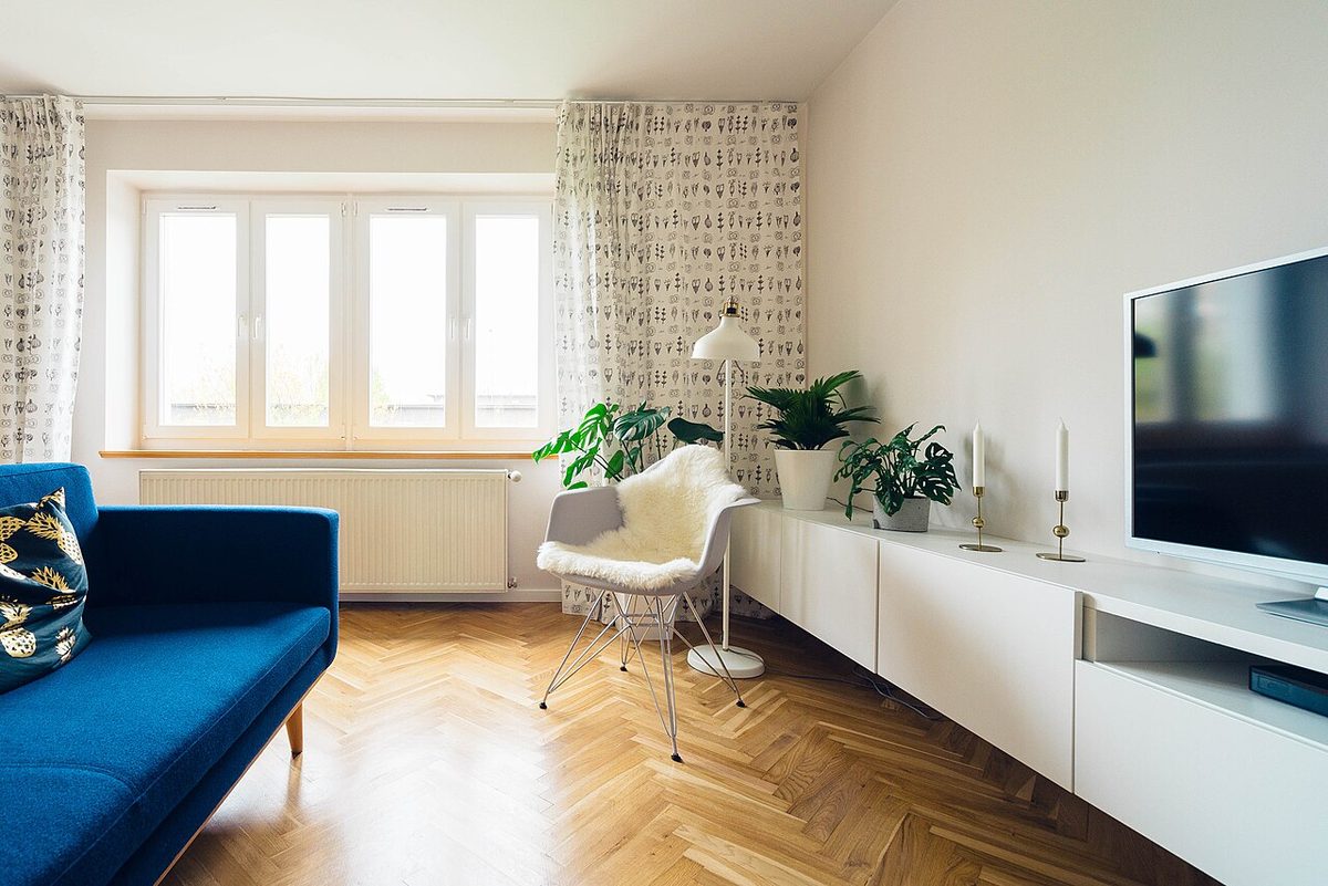 Illustrative stock photo: a bright, tidy living room with a window, plants and a wooden floor